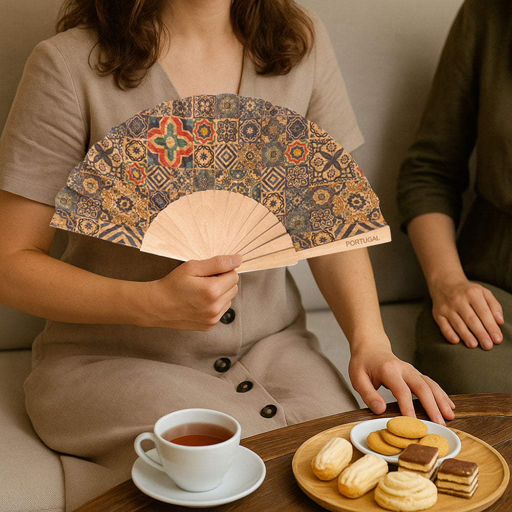 A LADY HAVING AFTERNOON TEA WITH FRIENDS, USING A COR FAN TO HAVE FRESH AIR